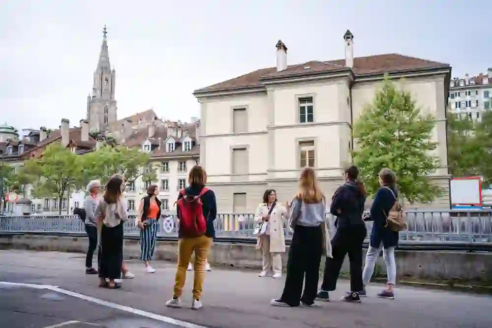 Interested listeners on a city tour in the Mattequartier, Bern, with the historical backdrop and tower of Bern Cathedral in the background.