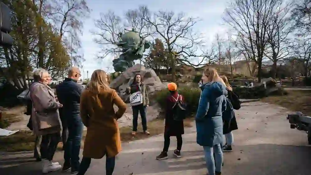 Die Tourteilnehmer stehen umgeben von Bäumen und Skulpturen, während sie den Worten des Führers folgen, eingetaucht in die fesselnde Erzählung der Stadtführung "1848 – Bern wird Bundesstadt" an einem hellen Tag.