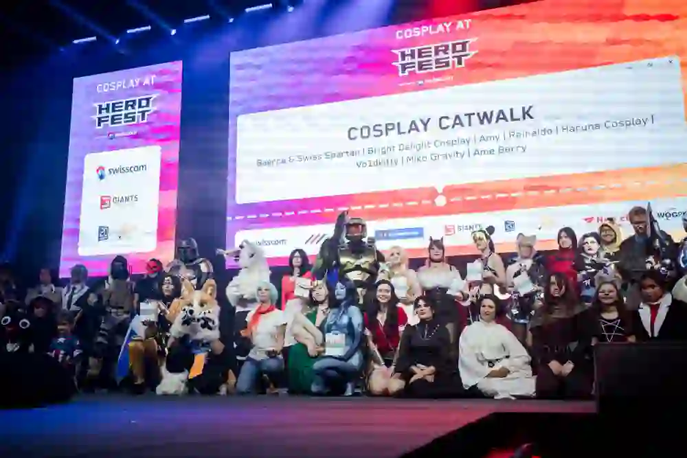 L'immagine mostra un gruppo di cosplayer su un palco durante un evento presumibilmente di grandi dimensioni nel padiglione Bernexpo di Berna.