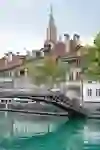 Ein idyllischer Blick auf das Mattequartier in Bern mit der Aare, einer Brücke und historischen Häusern, über denen das Berner Münster thront.