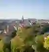 The picture shows a clear view of Bern with its historic city centre, church towers and rivers, framed by lively greenery under a wide blue sky, exuding a peaceful, picturesque atmosphere.