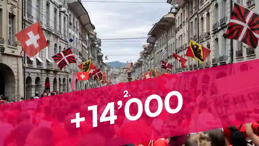 L'image montre une foule immense, vêtue de rouge et de blanc, traversant le pont Nydegg à Berne. L'ambiance est festive, unie et pleine d'énergie - probablement un événement sportif ou de fête nationale.