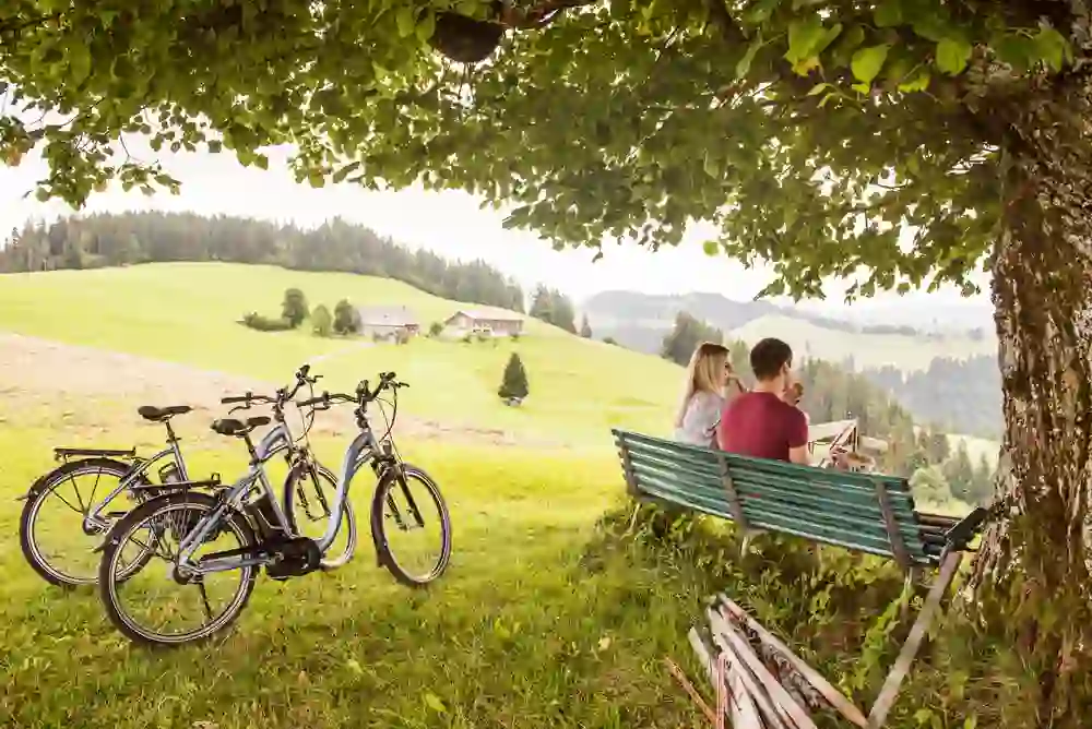 Ein Paar macht auf der Kambly Erlebnistour eine gemütliche Rast auf einer Bank, umgeben von der idyllischen Landschaft des Emmentals, mit Fahrrädern im Vordergrund.