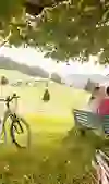 A couple take a cosy break on a bench on the Kambly adventure tour, surrounded by the idyllic landscape of the Emmental, with bicycles in the foreground.