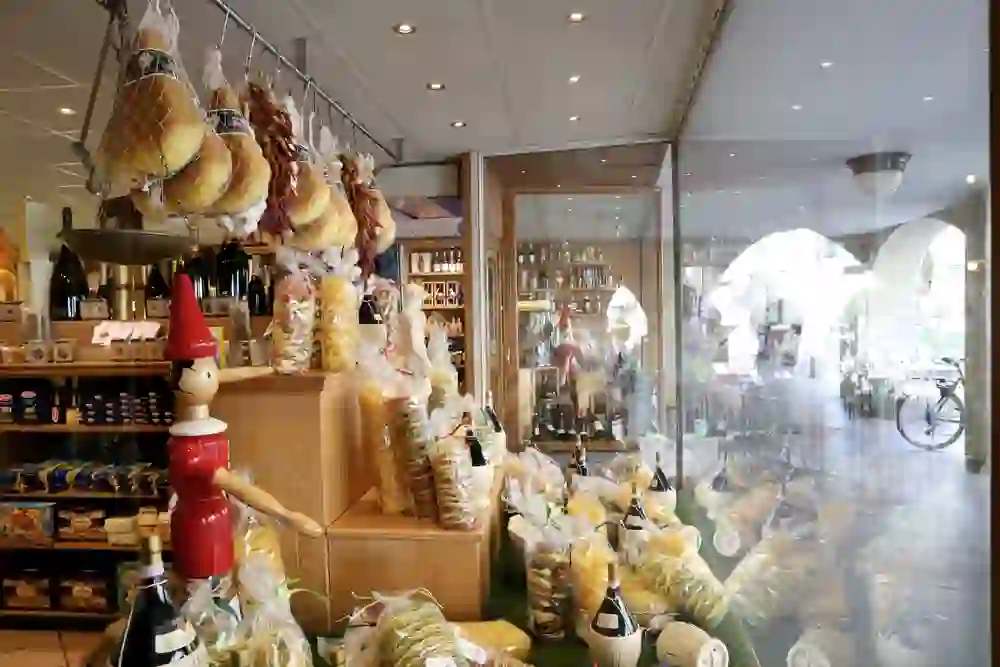 Das Bild zeigt das Innere eines Feinkostgeschäfts mit einer Vielzahl von Produkten, darunter Wurstwaren, Pasta und Weine. Die Ware ist ansprechend präsentiert und lädt zum Einkaufen ein. Das Geschäft kombiniert traditionelle Lebensmittel mit einer einladenden Atmosphäre.