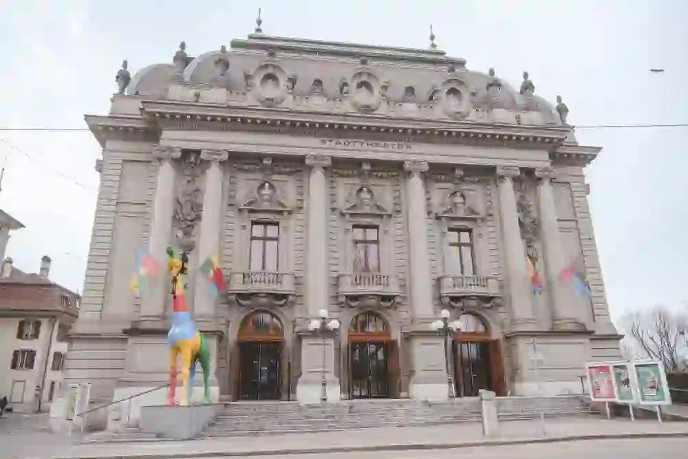 Vor dem imposanten Stadttheater Bern steht eine bunte, lebensgrosse Giraffen-Skulptur. Sie sorgt für einen spielerischen Kontrast zum klassischen Baustil des Theaters, dessen Eleganz und Tradition ausstrahlt. Die Giraffe bringt mit ihrem farbenfrohen Design Fröhlichkeit und Kreativität in die Szene, ein Symbol für die Vielfalt und Innovation, die in diesem Kulturhaus stattfinden.