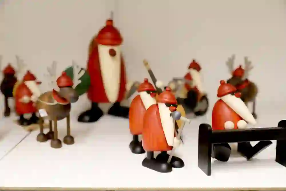 Auf dem Bild sind kunstvoll gestaltete Holzfiguren zu sehen, die vermutlich handgefertigte Dekorationsobjekte oder Spielzeuge sind. Sie haben die Form von Fantasiefiguren und Tieren, wie Elchen, mit auffälligen Farben und Details. Diese Figuren könnten in einem Handwerks- oder Kunstgeschäft ausgestellt sein.