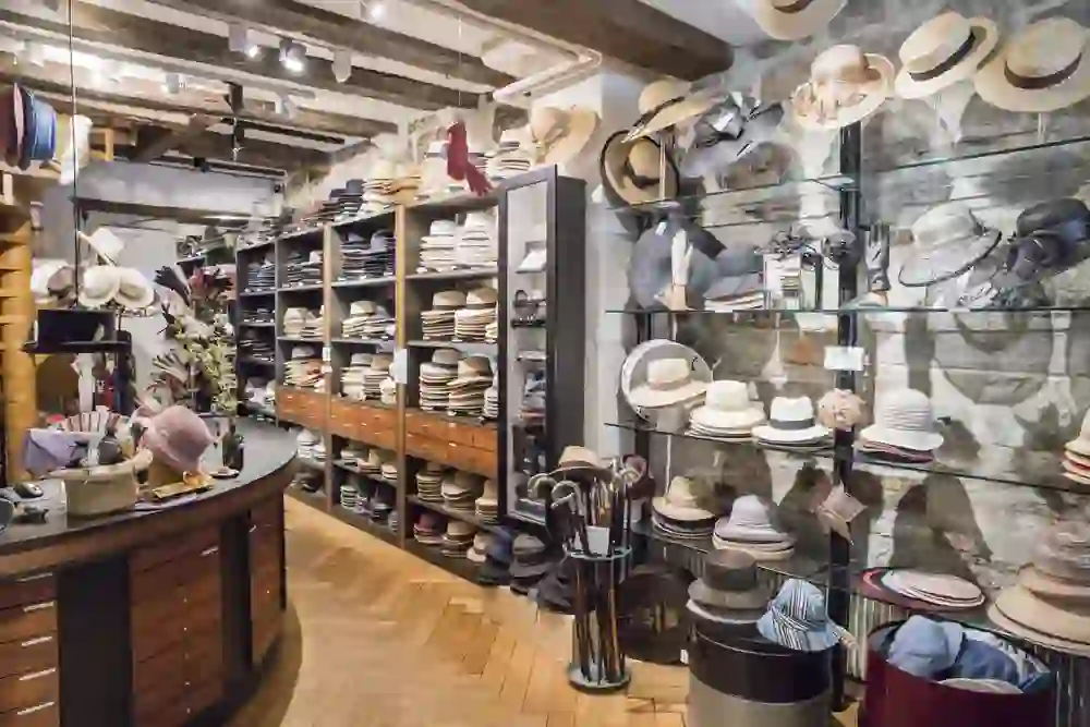 The picture shows the interior of a hat parlour with a large selection of hats displayed on shelves and in glass cabinets. The interior is stylish and combines modern and traditional elements.