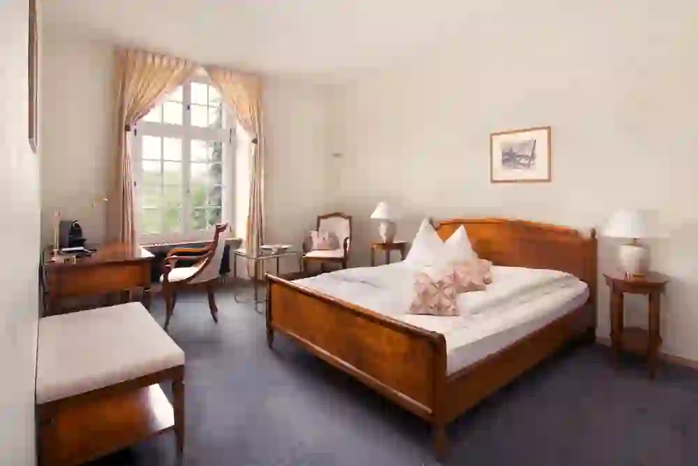 Auf dem Bild ist ein ordentliches und einladendes Schlafzimmer des Stadthauses Burgdorf  zu sehen. Es wirkt warm und gemütlich mit einem großen Bett, eleganten Möbeln und einem Fenster, das viel Licht hereinlässt.