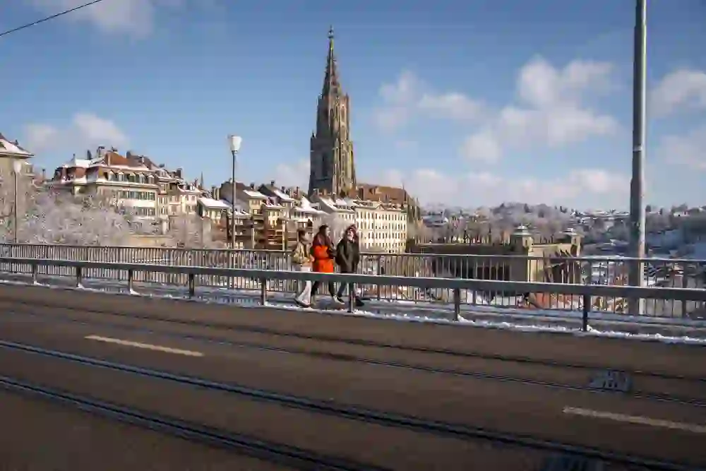 Zwei Personen geniessen den Blick auf das verschneite Bern und das Münster von der Kirchenfeldbrücke aus, eingehüllt in eine friedliche, winterliche Stille.
