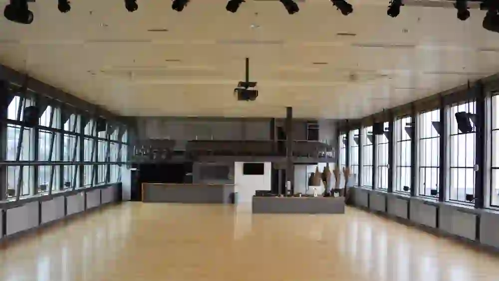 Une salle de réunion vide et spacieuse avec une grande baie vitrée. L'ambiance est silencieuse, en attente d'un événement ou d'un rassemblement à venir.