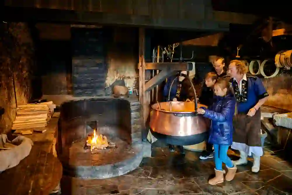A group watches in fascination as traditional cheese is made over an open fire, surrounded by a rustic ambience and warming glow.
