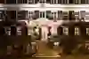 The image shows the night-time façade of a traditional hotel with illuminated windows and a staircase leading to an entrance with open doors. Flags adorn the exterior wall and the lighting gives the place a warm and inviting atmosphere.