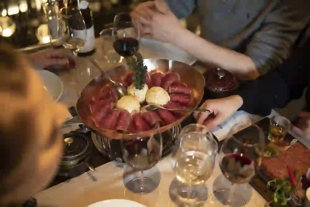 A convivial table scene in the Klösterli wine café with a platter full of red meat surrounded by glasses of wine creates an atmosphere of communal enjoyment and hospitality.