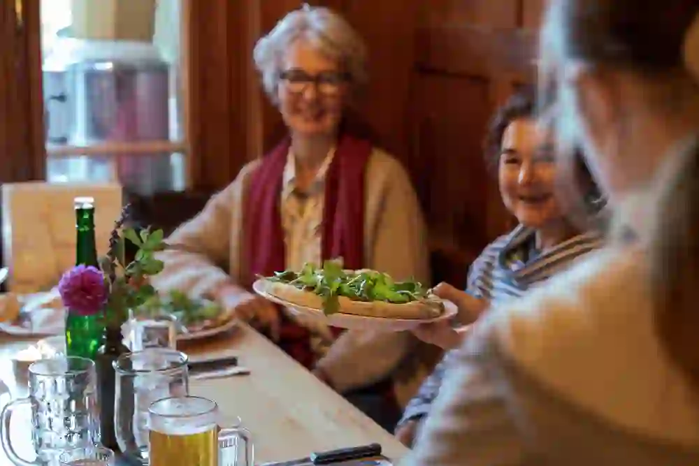 In der gemütlichen Atmosphäre der „Heiteren Fahne“ teilen lächelnde Gäste genussvoll eine frische Pizza, ein Moment des Glücks und der Verbundenheit.