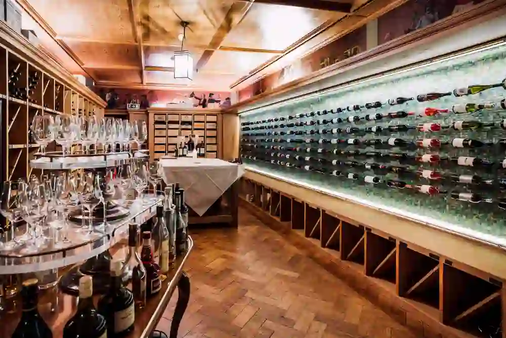 Das Bild zeigt den eleganten Innenraum eines Weinkellers mit einer beeindruckenden Anordnung von Weinflaschen und Gläsern. Die warme Beleuchtung und die Holzakzente schaffen eine einladende und luxuriöse Atmosphäre, ideal für genussvolle Weinverkostungen.