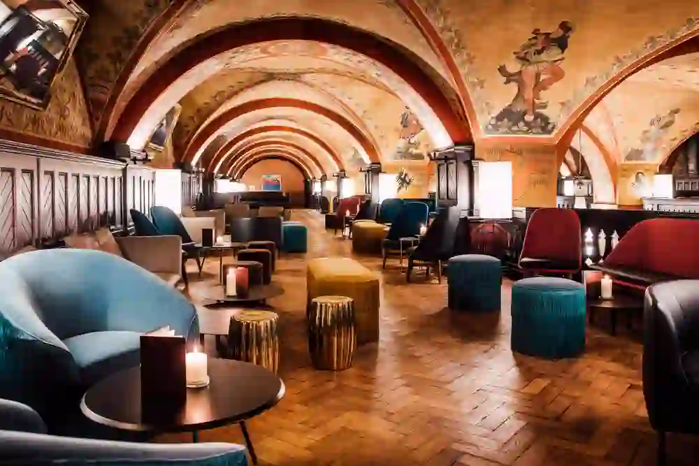 Das Bild zeigt das Innere der Bar Galerie im Kornhauskeller in Bern. Die historische Umgebung mit Gewölbedecken, die mit kunstvollen Malereien verziert sind, bietet eine atemberaubende Kulisse.