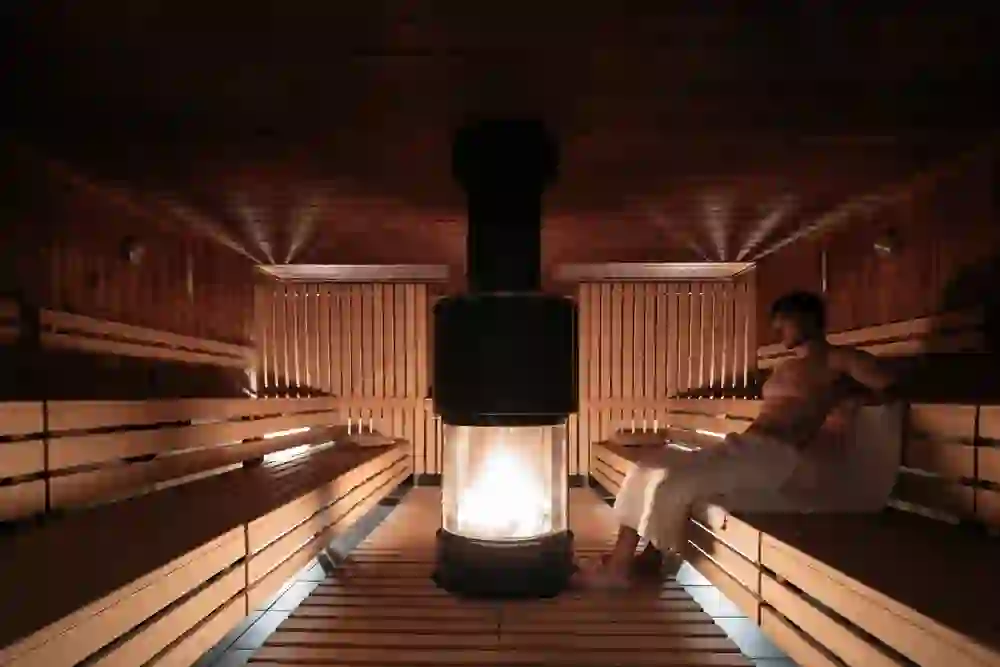 In der Sauna des Solbad & Spa Schönbühl findet sich ein Mann in tiefer Entspannung, umgeben von warmen Holztönen und dem sanften Schein des Feuers im Zentrum. Die Atmosphäre ist ruhig und erholsam.