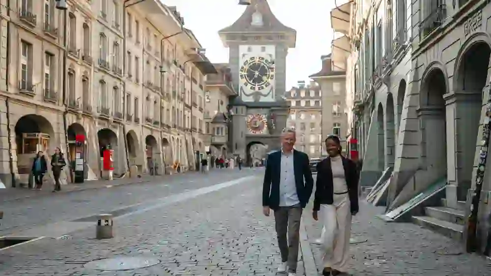 Zwei stilvoll gekleidete Personen schlendern entspannt durch die Berner Altstadt Richtung Zytglogge. Warmes Licht, historische Fassaden und Kopfsteinpflaster schaffen eine ruhige, inspirierende Atmosphäre zwischen urbaner Eleganz und zeitloser Geschichte.