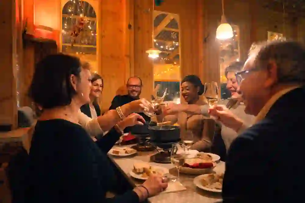 Gemütlicher Abend in warmem Chalet-Ambiente: Eine fröhliche Runde genießt Fondue, lacht und stößt mit Wein an – festliche Stimmung, gutes Essen und herzliche Gemeinschaft.