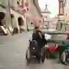 L'image montre des personnes en fauteuil roulant explorant le centre-ville animé, avec son architecture historique et ses drapeaux suisses. L'atmosphère est vivante et inclusive, avec un sentiment de communauté et d'accessibilité.