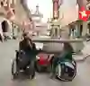 The picture shows people in wheelchairs exploring the bustling city centre with its historic architecture and Swiss flags. The atmosphere is lively and inclusive, with a sense of community and accessibility.