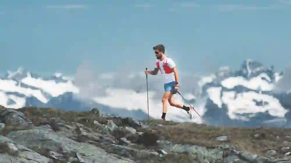 A sporty trail runner scales a rocky mountain path with full energy against a breathtaking mountain backdrop. The clear mountain air, the vastness of nature and the focus on the next step convey freedom, strength and pure joie de vivre.