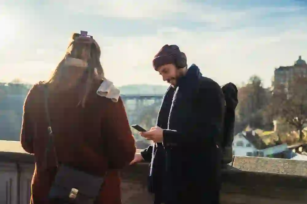 Hoch über der Aare stehen zwei Personen an der Mauer, der Blick in die Ferne gerichtet. Zwischen warmem Sonnenlicht und städtischem Panorama wird die Audiotour zum persönlichen Erlebnismoment.