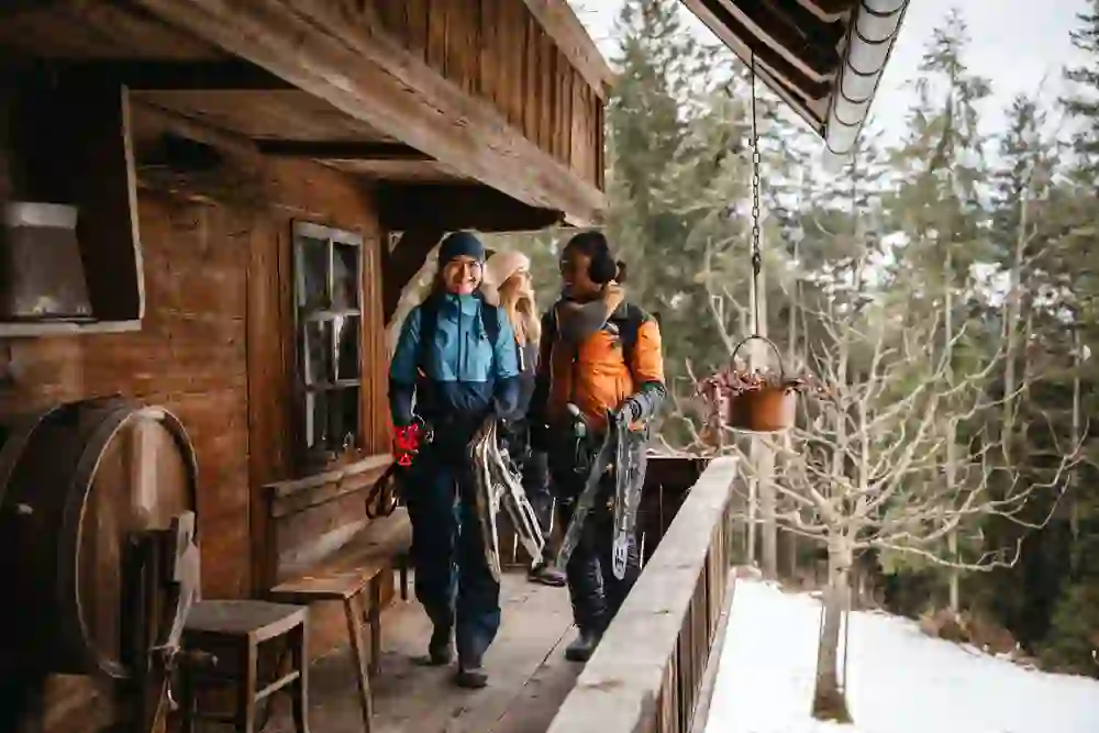 Three women reach the Sahlenweidli in Röthenbach in Emmental after a snowshoe tour. They laugh and look forward to a cosy get-together in the historic Sahlenweidli.