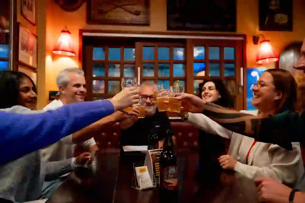 The picture shows a group of people clinking glasses of beer in a classic British pub in the city of Bern as part of a city tour on the subject of pub beer tours.