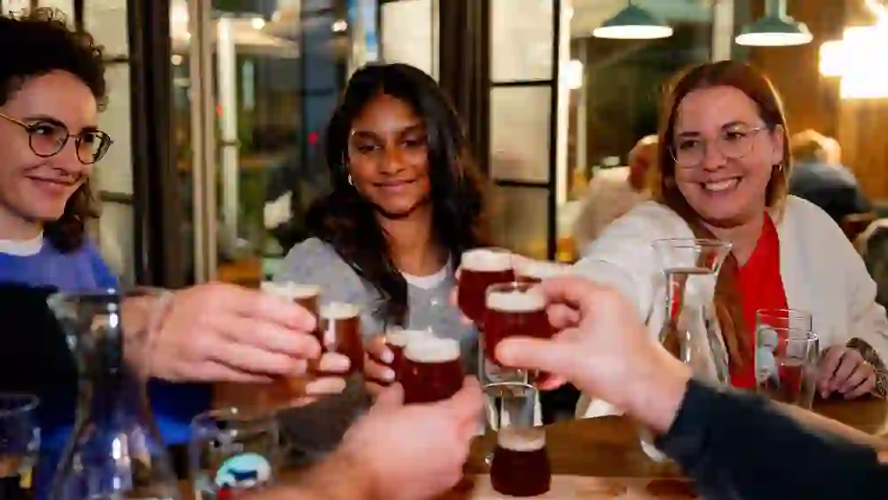 The picture shows a group of people clinking glasses of beer in a classic British pub in the city of Bern as part of a city tour on the subject of pub beer tours.