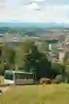 Une vue panoramique de la ville de Berne avec l'Aar, encadrée de collines verdoyantes. Au premier plan, le funiculaire du Gurten gravit la pente tandis qu'un bovin écossais des Highlands broute paisiblement dans la prairie.