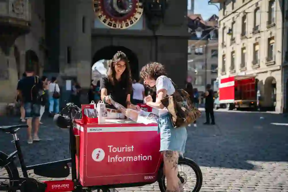 L'immagine mostra la TI sulla strada con una mappa e 2 persone davanti allo Zytglogge.