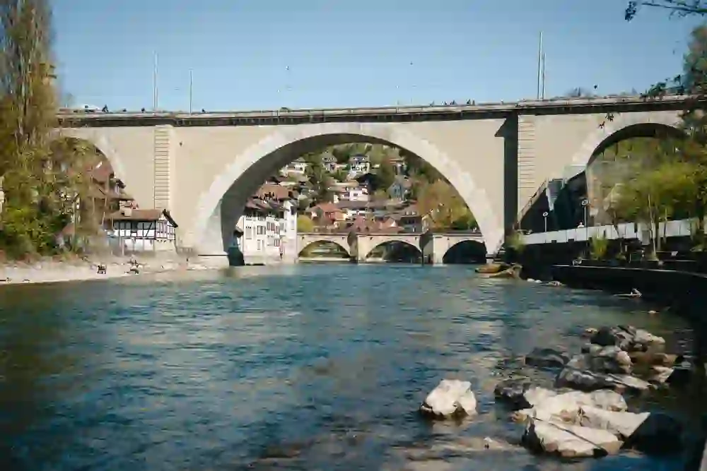 Sous l'imposante arche de pierre du pont de Nydegg, l'Aar scintille au soleil. Des gens s'attardent sur la rive, tandis que derrière le pont, le quartier pittoresque se blottit contre la pente. La scène respire le calme - un moment entre le bruit de l'eau et l'idylle urbaine.