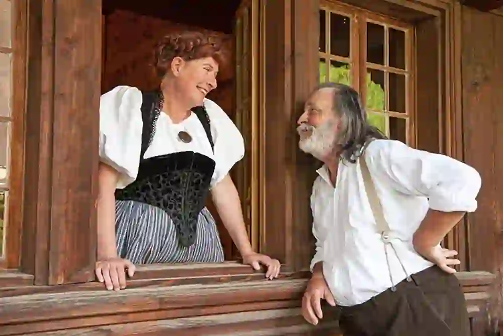 Das Bild zeigt zwei Personen in traditioneller Kleidung, die sich in einem herzlichen, ungezwungenen Gespräch befinden. Es handelt sich um eine Szene aus den Freilichtspielen, welche auf dem Gelände des Hotel Moosegg stattfinden.