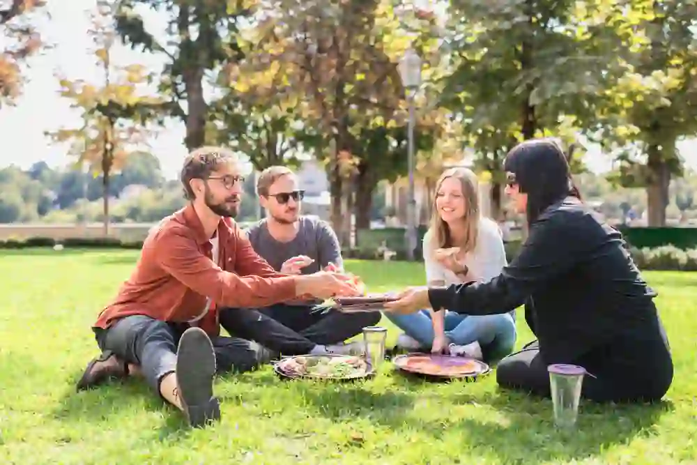 Un groupe joyeux profite d'un pique-nique durable sur la pelouse par un temps ensoleillé, en utilisant des récipients Recircle qui respirent la joie et la conscience écologique.