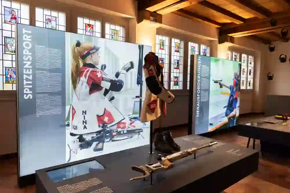 Sports equipment and photographs take centre stage in a bright exhibition room. Jerseys, rifles and shoes tell of precision and passion. The atmosphere is concentrated, respectful and arouses admiration for sporting excellence.
