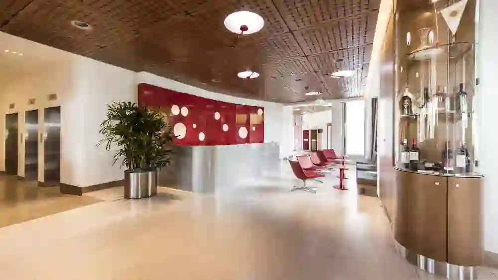 Das Bild zeigt die geräumige und stilvolle Lobby des Hotel Ambassador, die mit ihrem klaren Design und den leuchtenden Farbakzenten eine moderne und einladende Atmosphäre schafft.