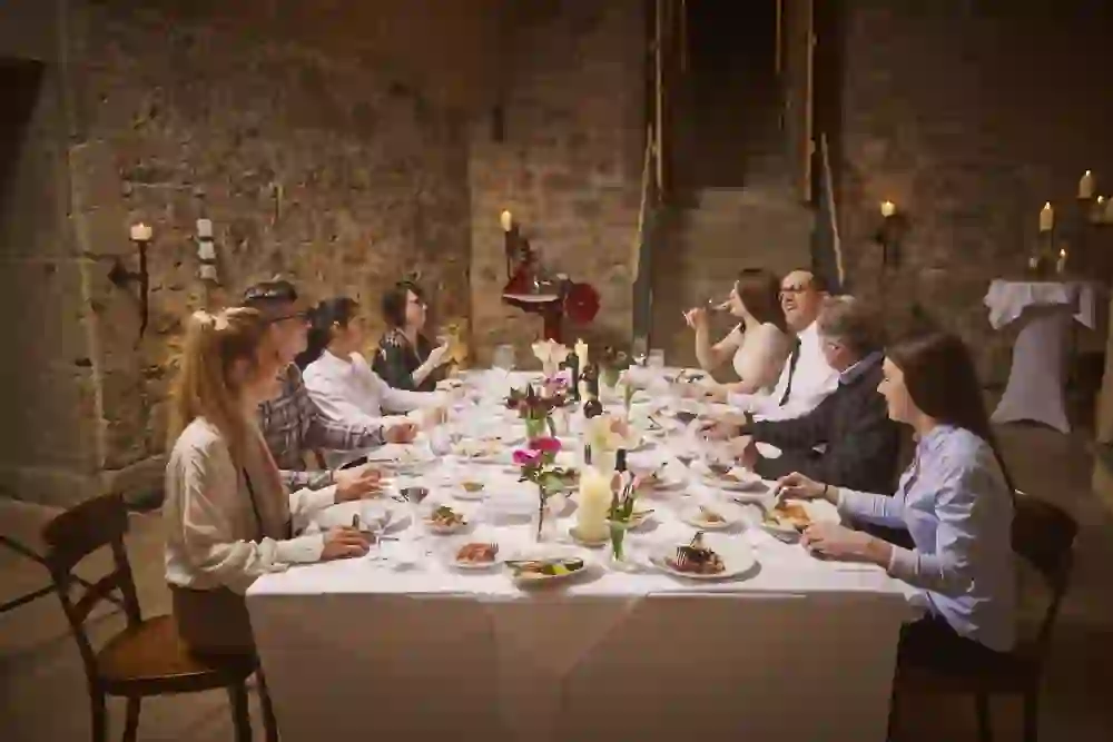 Das Bild zeigt eine fröhliche Gruppe, die im rustikalen Ambiente des Restaurant Verdi in Bern an einer langen Tafel sitzt, umgeben von warmem Kerzenlicht und Steinwänden, was ein Gefühl von Gemütlichkeit und Gemeinschaft vermittelt.