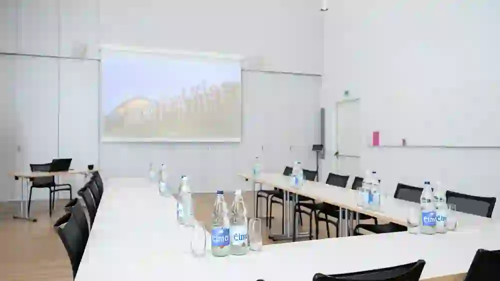 Una sala seminari vuota del Centro Paul Klee con tavoli e sedie ordinati. La proiezione indica la sua funzione di sede di eventi e congressi, creando un'atmosfera di attesa.