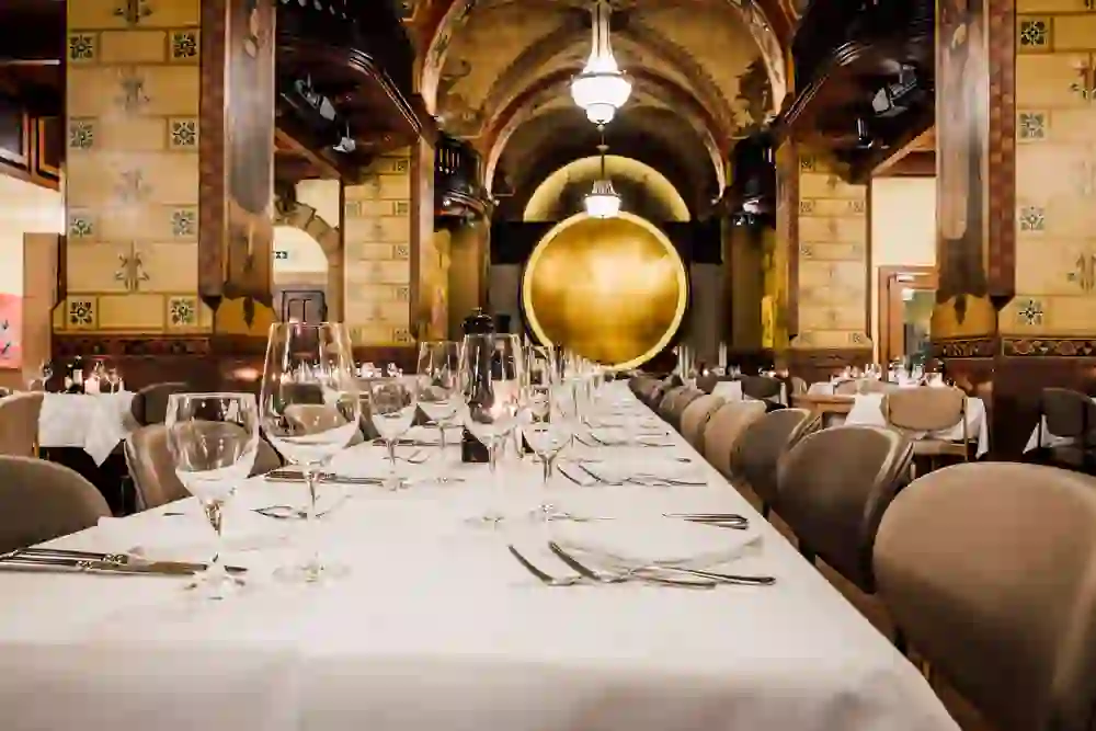 Das Bild zeigt einen eleganten Raum im Kornhauskeller in Bern, dominiert von einem grossen, runden Leuchtelement, das den Blick auf die feierlich gedeckten Tische und die historischen Wandmalereien lenkt, was eine einzigartige, stimmungsvolle Atmosphäre schafft.
