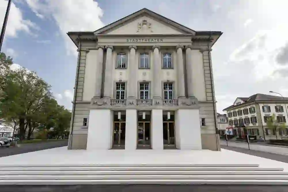 Das Bild zeigt das majestätische Stadttheater mit klassischer Architektur und Säulen, das unter klarem Himmel ruhig und erhaben wirkt, eine Einladung für Kulturbegeisterte, sich von Kunst und Performance inspirieren zu lassen.