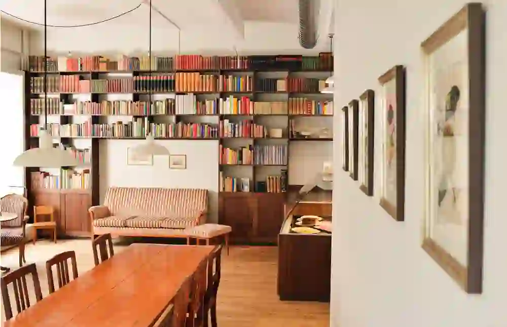 The picture shows a cosy café with a rich collection of books on the walls, bathed in warm, inviting light. The atmosphere is relaxed and inviting, perfect for reading lovers who want to enjoy a quiet environment.