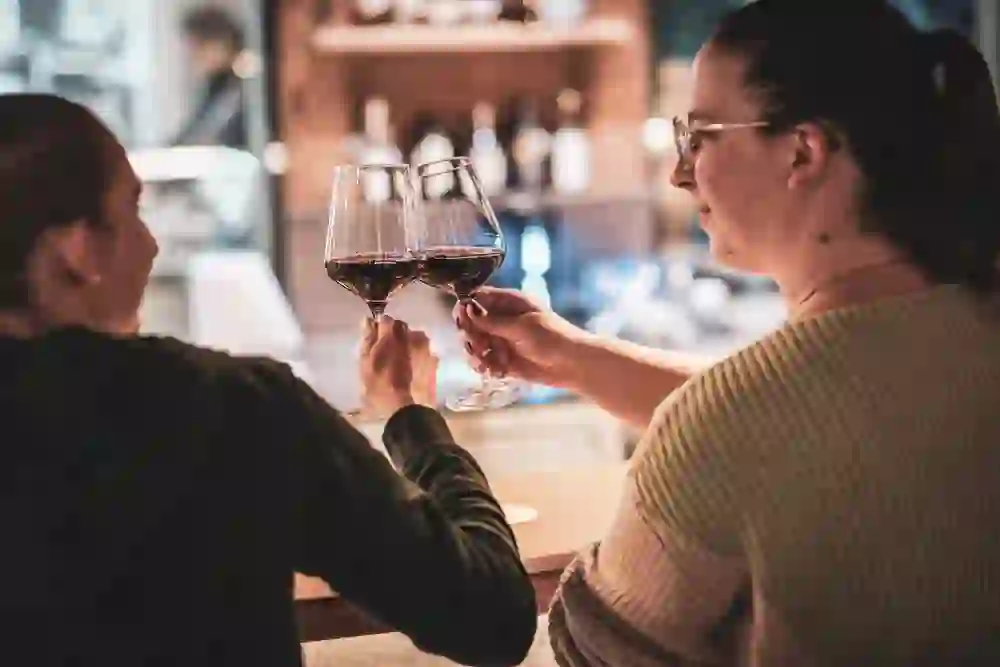Un momento di unione: due persone brindano davanti a un bicchiere di vino rosso - rilassato, familiare e caldo. L'illuminazione calda enfatizza l'ambiente accogliente.