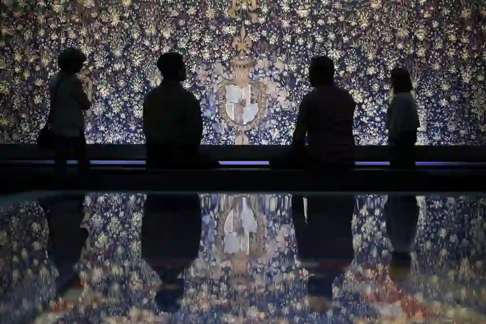 La photo montre des visiteurs d'une exposition au Musée historique de Berne, plongés dans la contemplation d'une magnifique œuvre d'art. L'environnement sombre et la lumière réfléchie créent une atmosphère respectueuse et presque méditative. Tous les visiteurs semblent plongés dans leurs pensées, comme si l'œuvre d'art les transportait dans un autre monde. L'ambiance calme et concentrée est encore renforcée par l'éclairage tamisé et les reflets au sol.