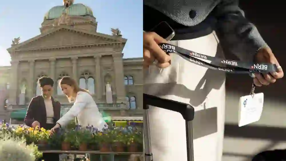 Zwei Personen betrachten Blumen vor dem Bundeshaus in Bern; warmes Sonnenlicht und ruhige Stadtszene. Rechts hält eine Person ein BERN-Lanyard mit Badge neben einem Koffer – ankommend, willkommen und organisiert.