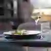 Un piatto di verdure e ortaggi su un tavolo, accompagnato da un bicchiere di vino bianco e da un bicchiere d'acqua, in un ristorante poco illuminato.