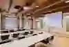 La salle donne une impression de calme, de clarté et de concentration. Les longues rangées de tables en forme de U créent une atmosphère structurée et propice au dialogue - idéale pour les réunions, les ateliers ou les séminaires. Les poutres en bois apparentes au plafond confèrent à la salle chaleur et caractère, tandis que les grandes fenêtres laissent entrer beaucoup de lumière du jour et rendent le contexte historique perceptible. Dans l'ensemble, il en résulte une interaction équilibrée entre fonctionnalité, discrétion et élégance intemporelle.
