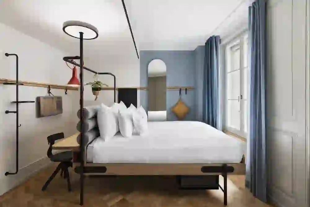Ein stilvolles Schlafzimmer mit einem bequemen Bett im Stay Kooook Bern City, akzentuiert durch blaue Vorhänge und Wanddetails, strahlt eine beruhigende und einladende Atmosphäre aus.