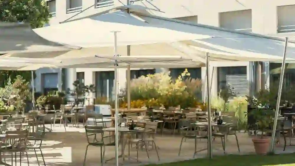 L'image montre la paisible terrasse extérieure d'un restaurant avec de grands parasols qui assurent l'ombre. L'atmosphère est relaxante et accueillante, parfaite pour un agréable repas en plein air.